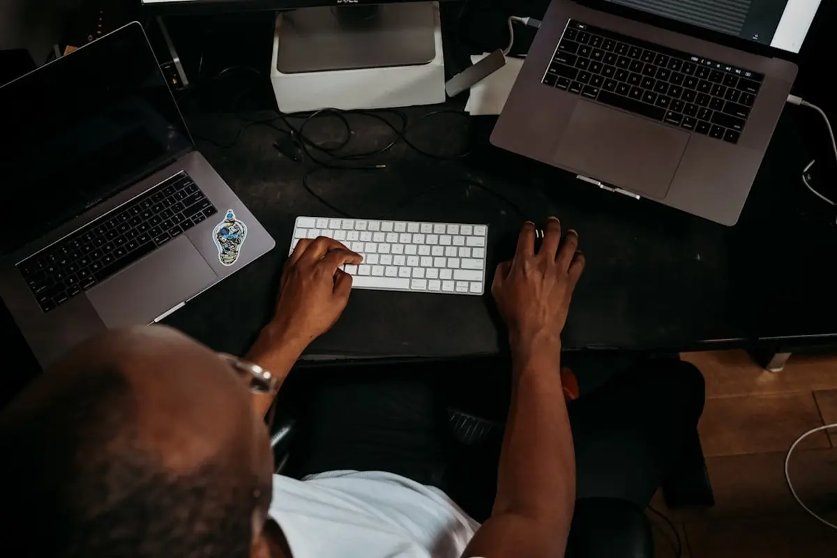 man standing and facing whiteboard with writings near woman pointing at it and facing man sitting beside table with laptop indoors