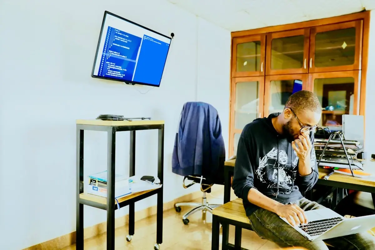 four people all on laptops, two men and two women, listen to person talking in a board meeting