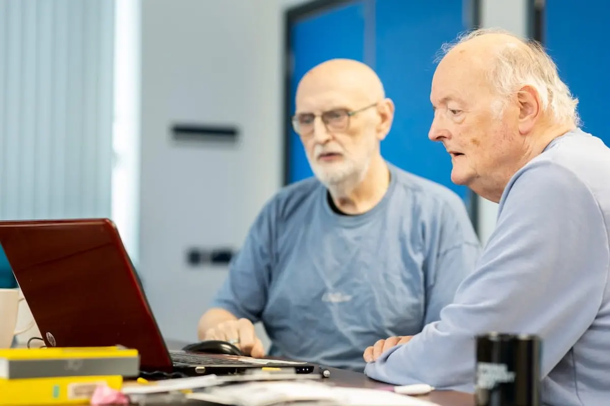 four people all on laptops, two men and two women, listen to person talking in a board meeting