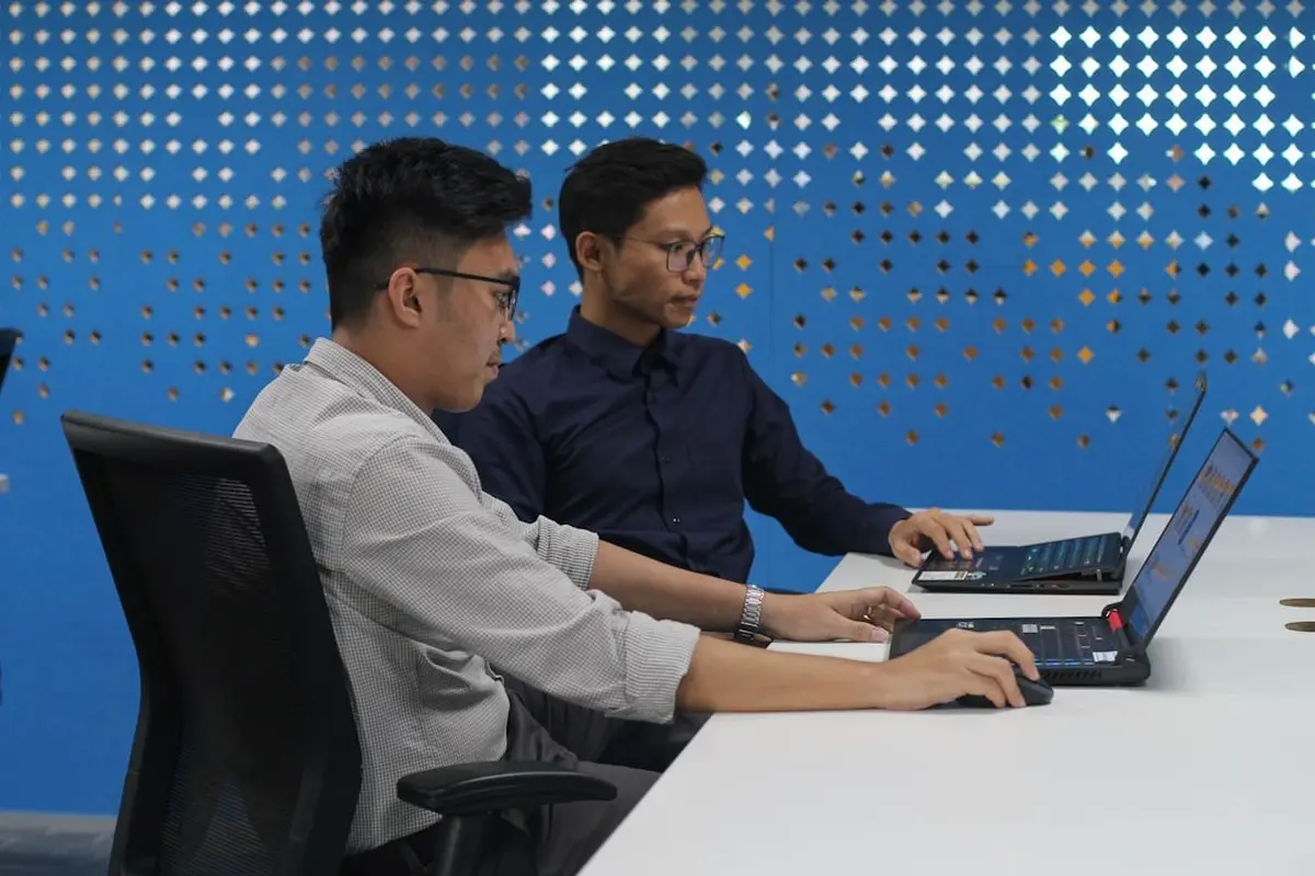 four people all on laptops, two men and two women, listen to person talking in a board meeting