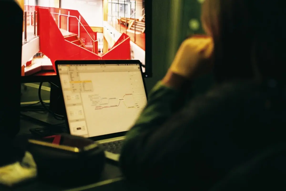 four people all on laptops, two men and two women, listen to person talking in a board meeting