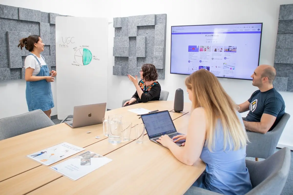 four people all on laptops, two men and two women, listen to person talking in a board meeting