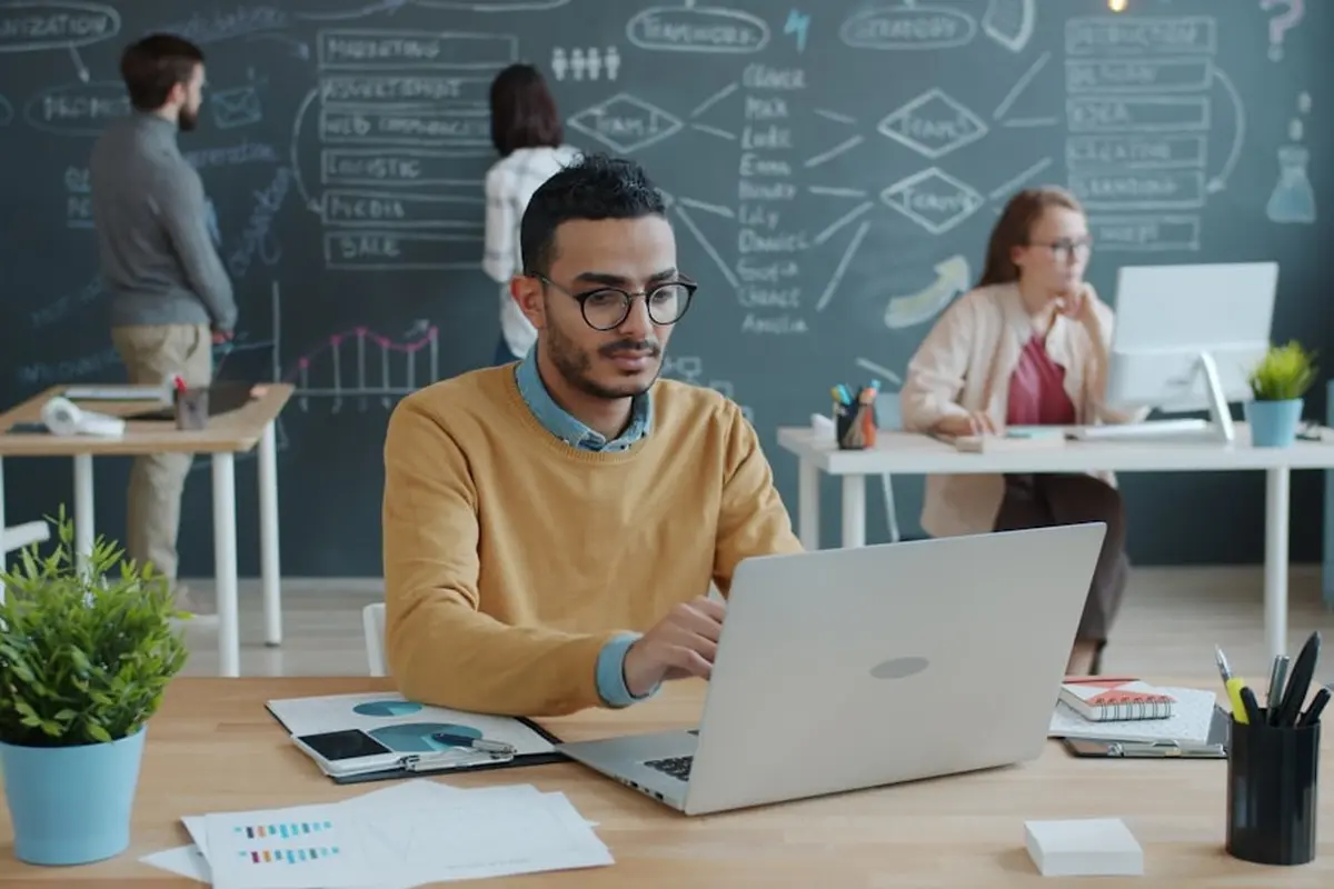 four people all on laptops, two men and two women, listen to person talking in a board meeting