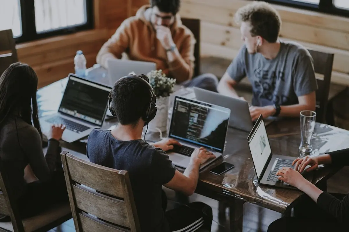 four people all on laptops, two men and two women, listen to person talking in a board meeting