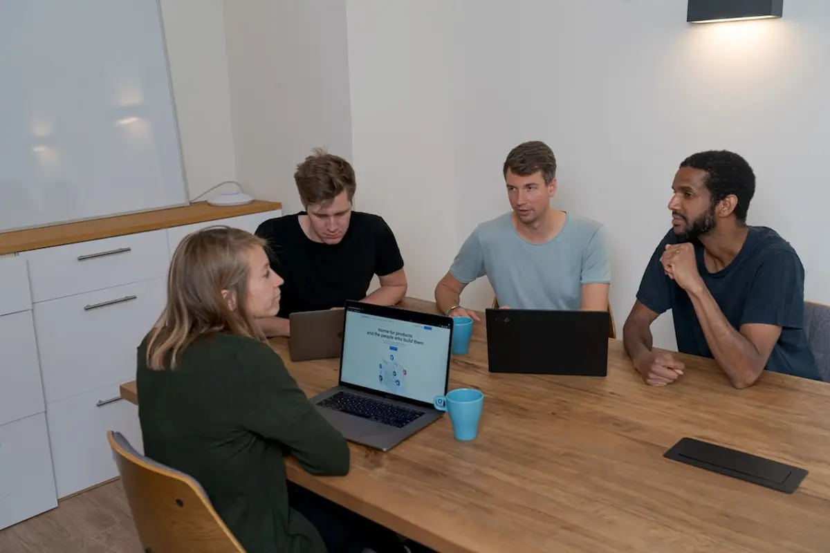 four people all on laptops, two men and two women, listen to person talking in a board meeting