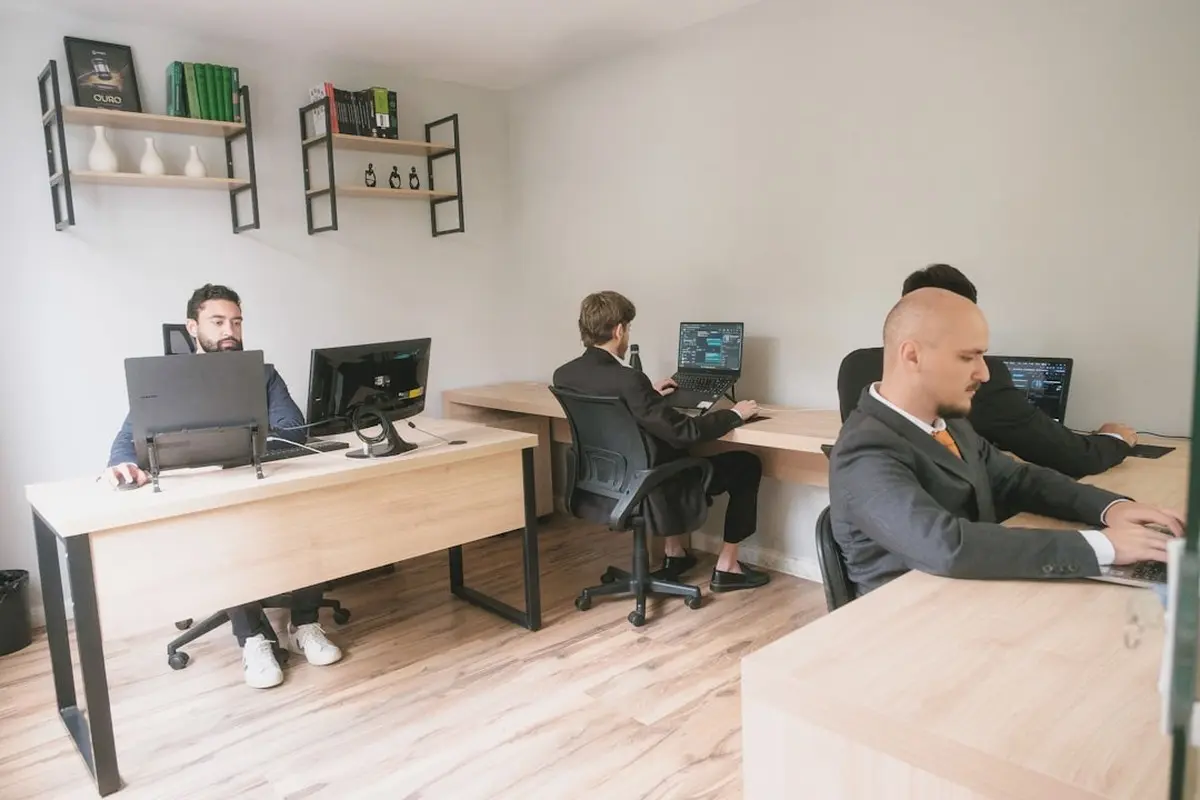 four people all on laptops, two men and two women, listen to person talking in a board meeting